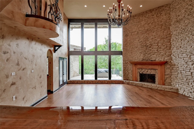 unfurnished living room with a high ceiling, wood-type flooring, a fireplace, and an inviting chandelier