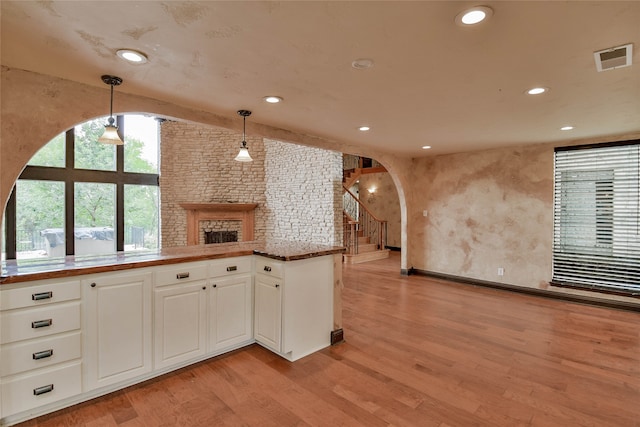 kitchen featuring light wood-type flooring, pendant lighting, white cabinetry, kitchen peninsula, and a stone fireplace