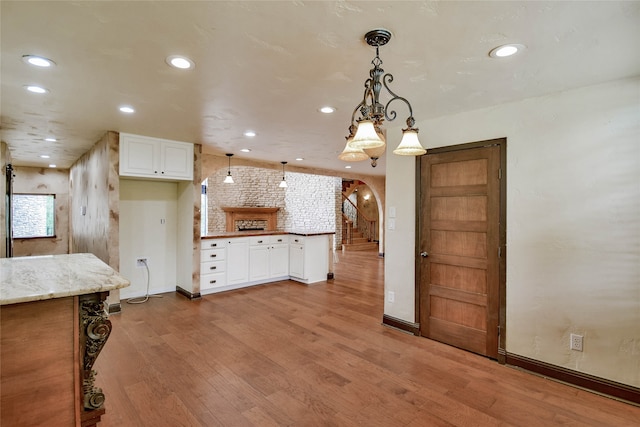 kitchen with brick wall, hanging light fixtures, light wood-type flooring, and white cabinets