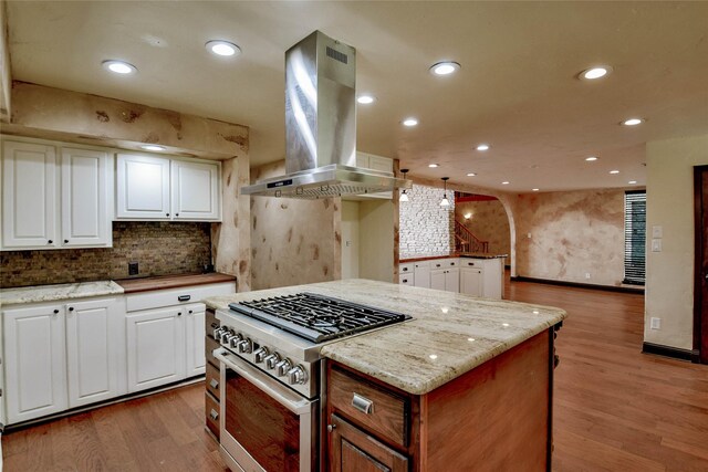 kitchen with stainless steel stove, wood-type flooring, island exhaust hood, white cabinetry, and light stone counters