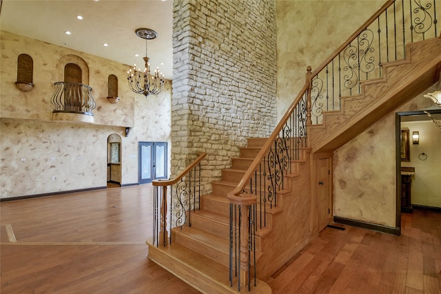 stairway with a chandelier, hardwood / wood-style floors, and a high ceiling