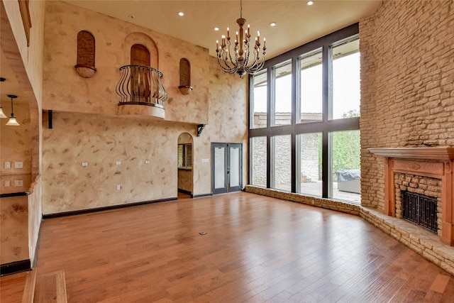 unfurnished living room featuring a high ceiling, a notable chandelier, a stone fireplace, and wood-type flooring