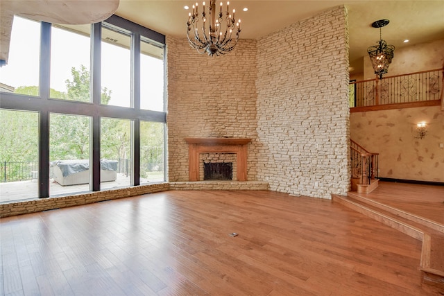 unfurnished living room with a notable chandelier, hardwood / wood-style floors, a towering ceiling, and a fireplace