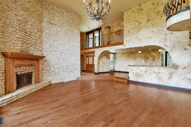 unfurnished living room featuring a high ceiling, hardwood / wood-style floors, a notable chandelier, and a stone fireplace