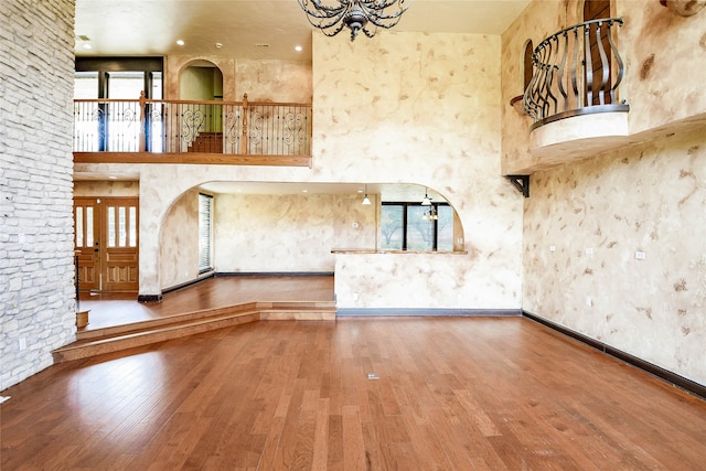 unfurnished living room featuring wood-type flooring, an inviting chandelier, and a towering ceiling