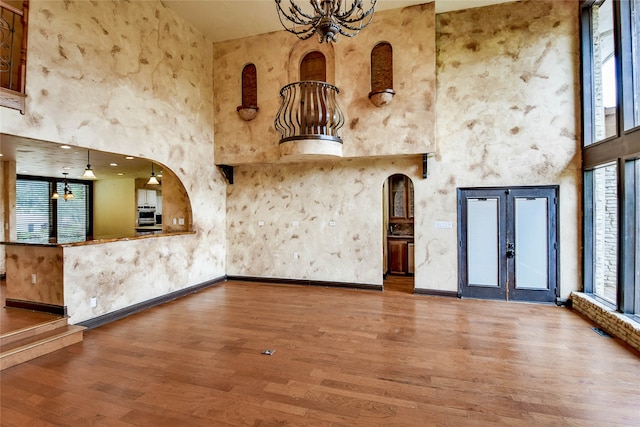 unfurnished room featuring a healthy amount of sunlight, hardwood / wood-style flooring, an inviting chandelier, and a towering ceiling