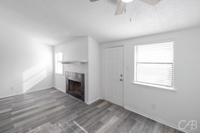 unfurnished living room featuring ceiling fan, wood-type flooring, a tile fireplace, and a textured ceiling