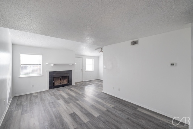 unfurnished living room with ceiling fan, a textured ceiling, wood-type flooring, and a tiled fireplace