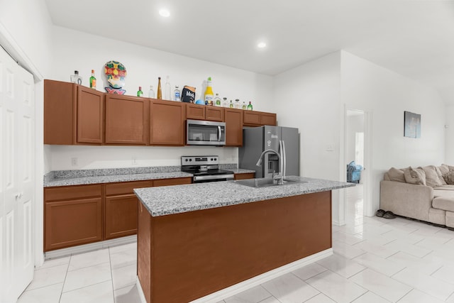 kitchen with light tile patterned flooring, stainless steel appliances, an island with sink, sink, and light stone countertops