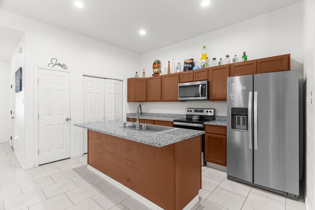 kitchen featuring sink, appliances with stainless steel finishes, light tile patterned floors, and a center island with sink