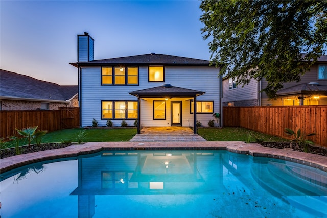 back house at dusk featuring a yard and a fenced in pool