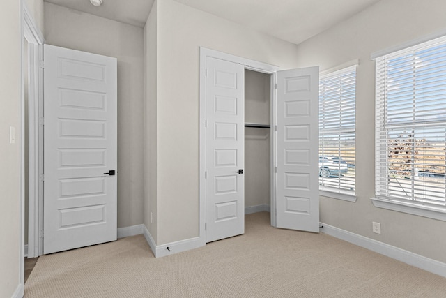 unfurnished bedroom featuring multiple windows, light carpet, and a closet