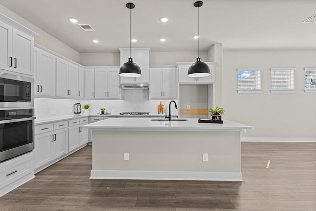 kitchen featuring stainless steel oven, a kitchen island with sink, and white cabinets