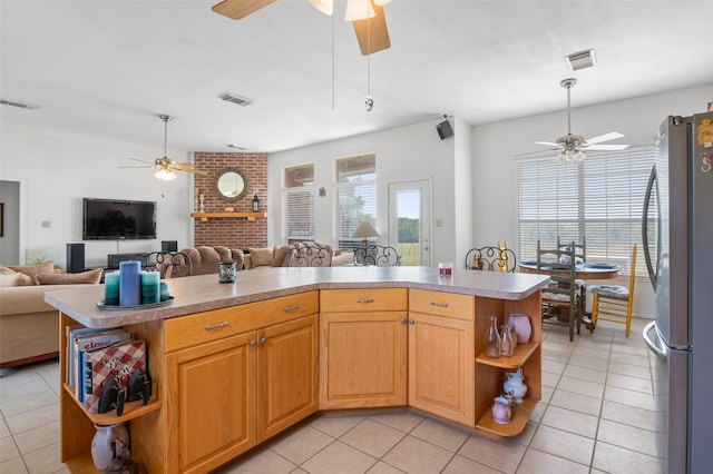 kitchen with light tile patterned flooring, ceiling fan, brick wall, and stainless steel refrigerator