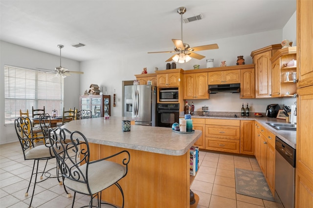 kitchen with light tile patterned flooring, a center island, appliances with stainless steel finishes, a kitchen breakfast bar, and ceiling fan