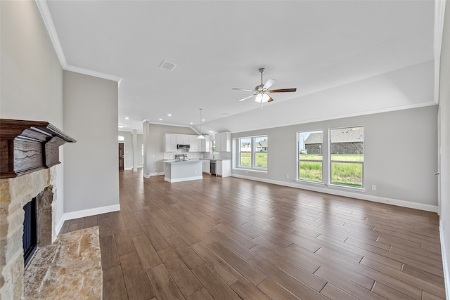 unfurnished living room featuring hardwood / wood-style flooring, a stone fireplace, ornamental molding, and ceiling fan