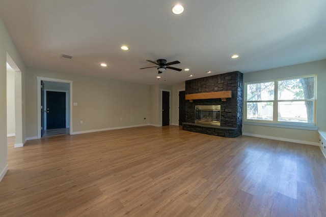 unfurnished living room with ceiling fan, a stone fireplace, and hardwood / wood-style floors