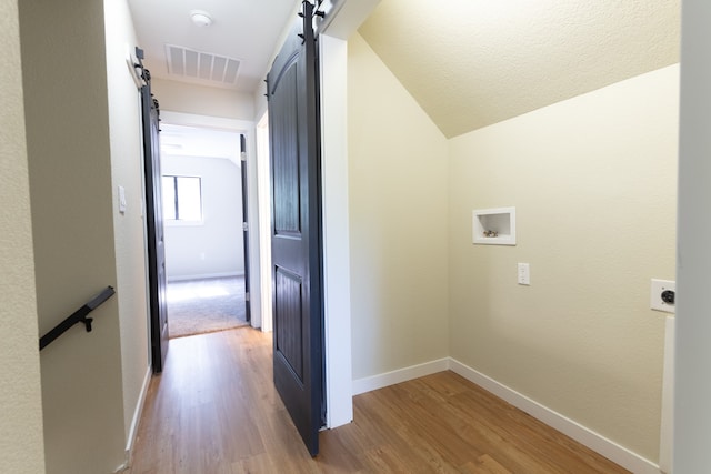 corridor with light hardwood / wood-style floors, lofted ceiling, and a barn door