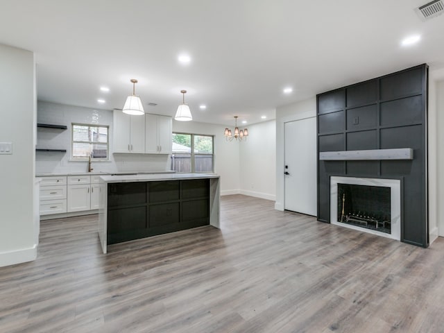 kitchen featuring a kitchen island, decorative light fixtures, a fireplace, light hardwood / wood-style floors, and white cabinetry