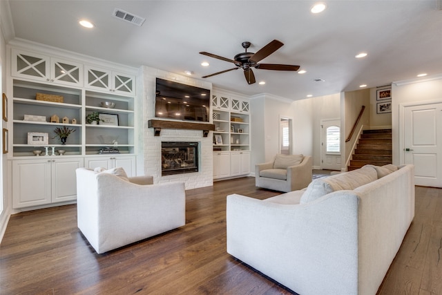 living room with built in features, hardwood / wood-style floors, crown molding, a brick fireplace, and ceiling fan