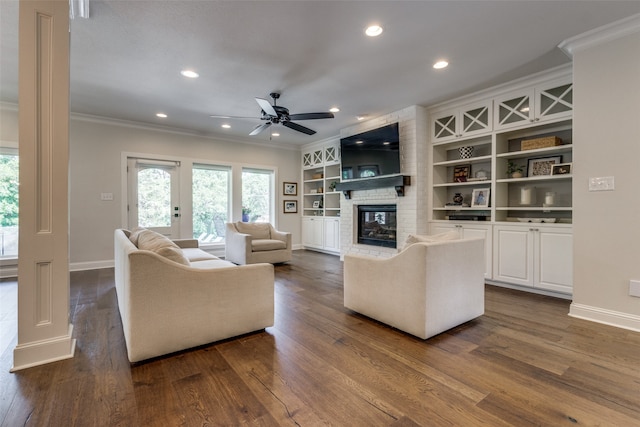 living room with a fireplace, ceiling fan, built in features, ornamental molding, and dark wood-type flooring