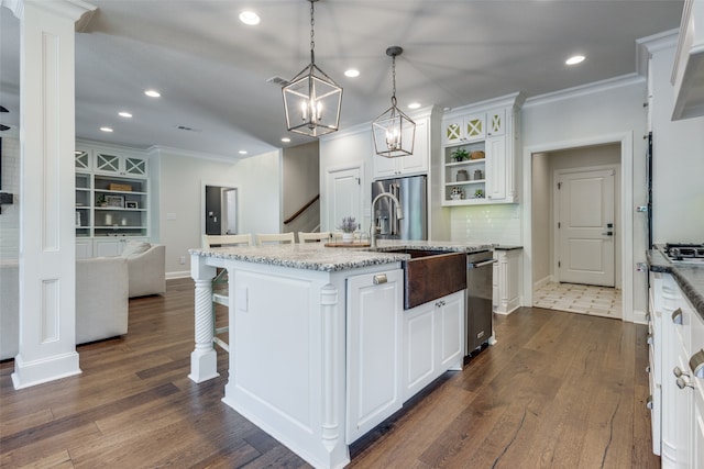 kitchen featuring appliances with stainless steel finishes, dark tile patterned floors, white cabinets, decorative backsplash, and an island with sink