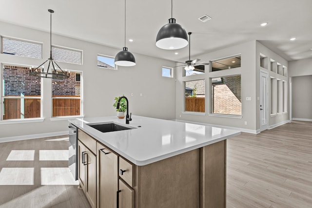 kitchen featuring an island with sink, sink, hanging light fixtures, stainless steel dishwasher, and light hardwood / wood-style flooring