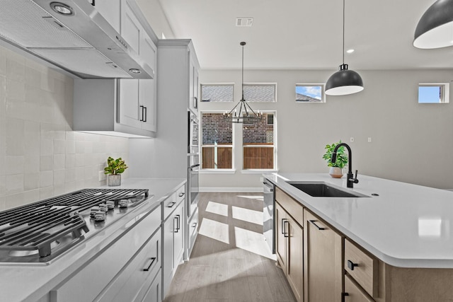 kitchen with wall chimney range hood, sink, appliances with stainless steel finishes, backsplash, and decorative light fixtures