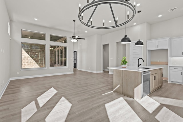 kitchen with decorative light fixtures, white cabinetry, stainless steel dishwasher, light hardwood / wood-style floors, and a center island with sink