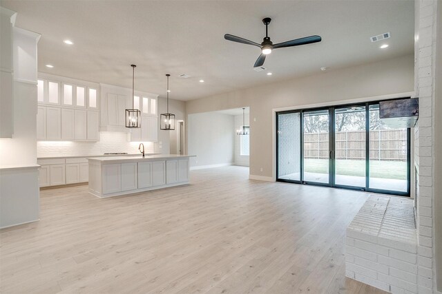 kitchen with hanging light fixtures, appliances with stainless steel finishes, a kitchen island with sink, and white cabinets