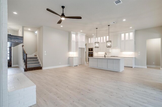 kitchen with white cabinetry, black microwave, an island with sink, pendant lighting, and stainless steel double oven