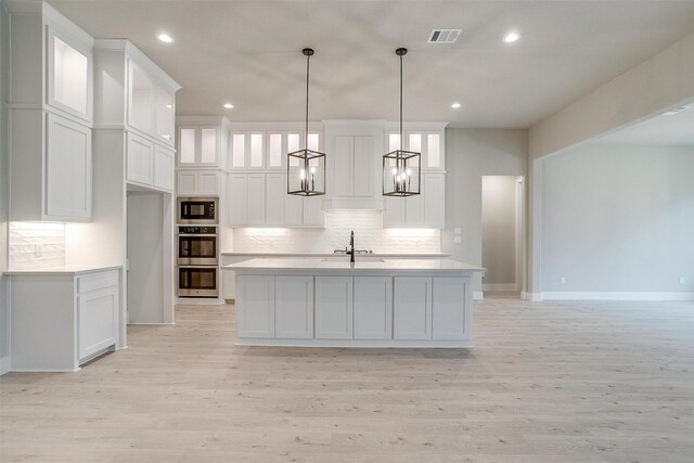 kitchen featuring sink, white cabinets, a center island with sink, a brick fireplace, and decorative light fixtures