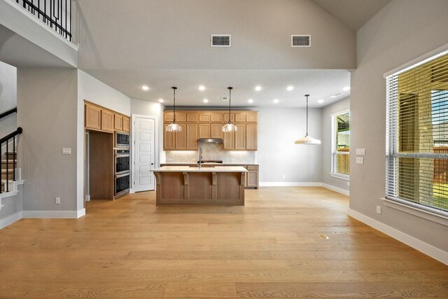 kitchen with light hardwood / wood-style floors, decorative backsplash, a center island with sink, and decorative light fixtures