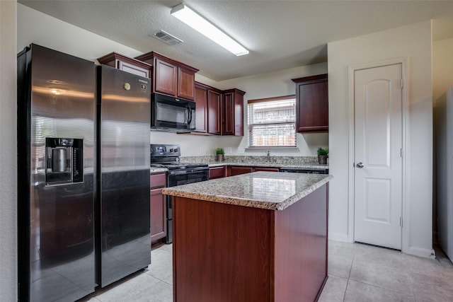 311 Soap Tree Dr, Princeton, TX 75407 - kitchen with black appliances, light tile patterned floors, a kitchen island, light stone countertops, and a textured ceiling
