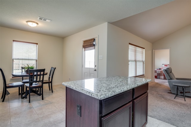 kitchen featuring a center island, light stone countertops, dark brown cabinetry, lofted ceiling, and light tile patterned floors