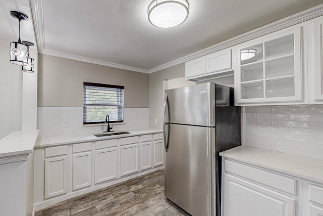 kitchen featuring sink, white cabinets, stainless steel refrigerator, light hardwood / wood-style flooring, and ornamental molding