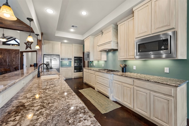 kitchen featuring cream cabinetry, stainless steel appliances, light stone counters, and custom range hood