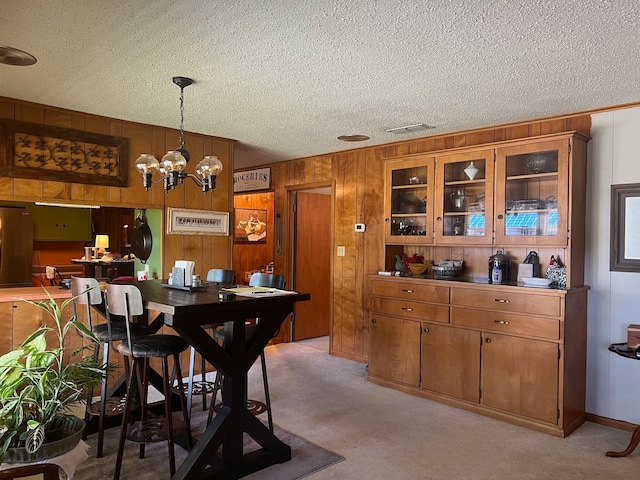 dining space featuring wood walls, light carpet, a notable chandelier, and a textured ceiling