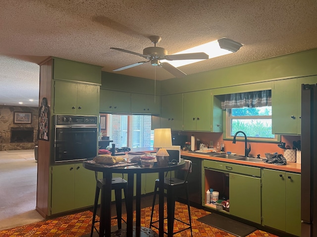 kitchen featuring sink, green cabinets, light carpet, ceiling fan, and black oven