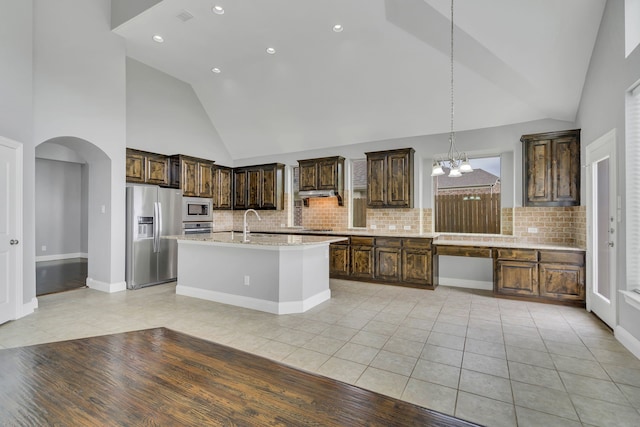 kitchen featuring appliances with stainless steel finishes, decorative light fixtures, light tile patterned floors, light stone countertops, and dark brown cabinets