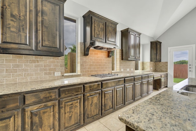 kitchen featuring stainless steel gas cooktop, vaulted ceiling, dark brown cabinets, light tile patterned floors, and decorative backsplash