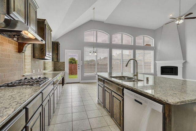 kitchen featuring appliances with stainless steel finishes, sink, a large fireplace, a kitchen island with sink, and light stone counters