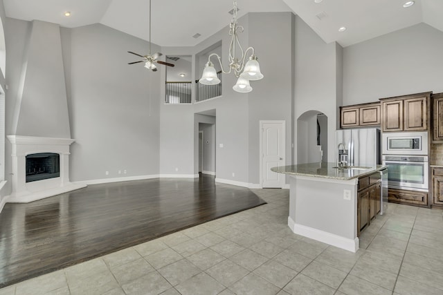 kitchen with light stone countertops, appliances with stainless steel finishes, a kitchen island with sink, and light tile patterned flooring