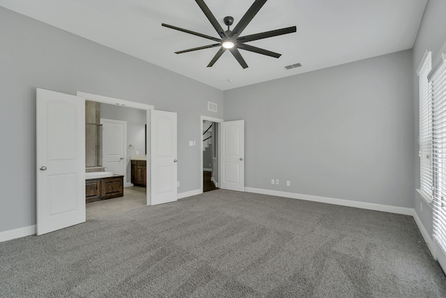 unfurnished bedroom featuring ceiling fan, multiple windows, ensuite bath, and light carpet