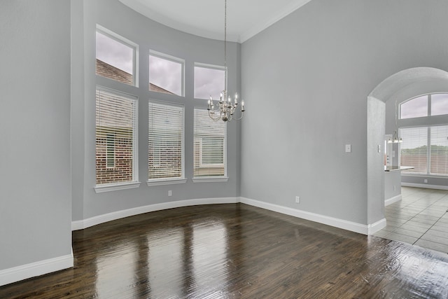 spare room featuring crown molding, dark wood-type flooring, and an inviting chandelier