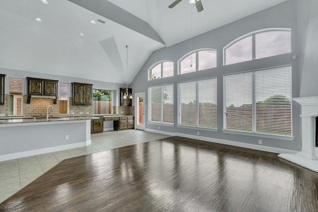 unfurnished living room with light tile patterned flooring, ceiling fan, sink, and high vaulted ceiling