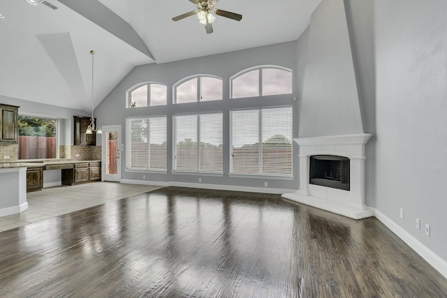 unfurnished living room with hardwood / wood-style flooring, a fireplace, high vaulted ceiling, and ceiling fan