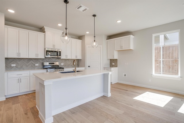 kitchen with appliances with stainless steel finishes, white cabinets, sink, and an island with sink