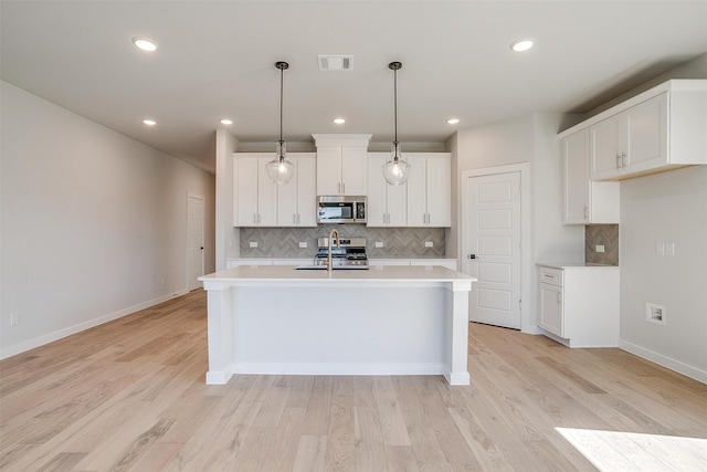 kitchen with light hardwood / wood-style flooring, a center island with sink, decorative light fixtures, white cabinetry, and appliances with stainless steel finishes