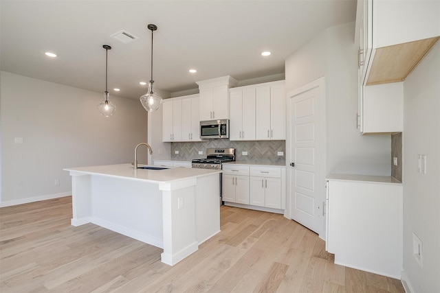 kitchen with sink, white cabinetry, light hardwood / wood-style floors, stainless steel appliances, and decorative light fixtures